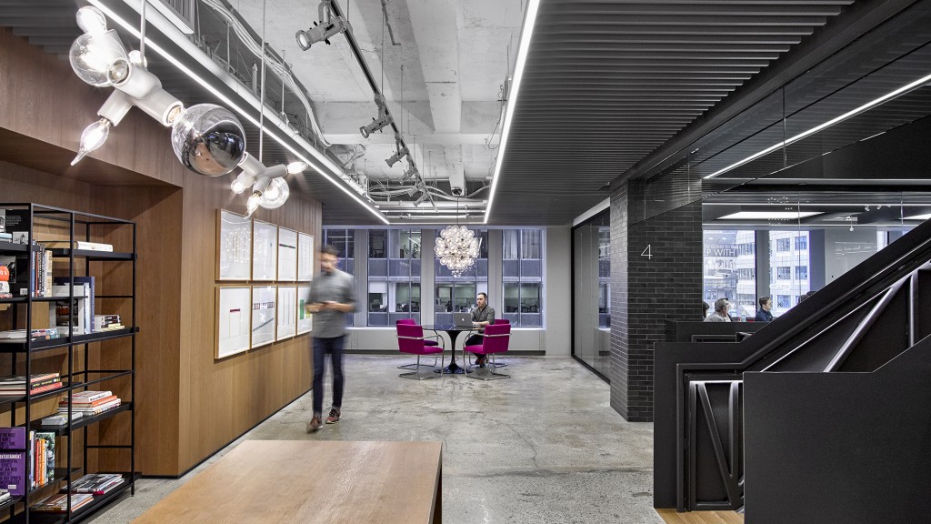 A person standing in a room with a large screen and shelves with books.